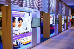 An image of the interior of the new UOIT booth at the Ontario Universities Fair, with large, backlit graphic panels and flat-screen displays.