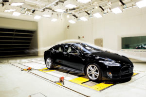 A black Tesla car under bright heat lights in the ACE climatic wind tunnel, with a stream of smoke indicating the flow of wind over the vehicle.