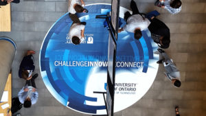 An overhead view of people walking across a circular, abstract floor graphic installed in a university building's atrium.